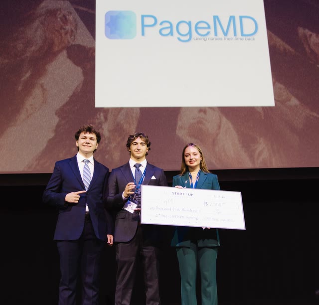 Seth and his two PageMD teammates on stage at the STARTedUP Challenge, holding the prize check in front of the PageMD slide
